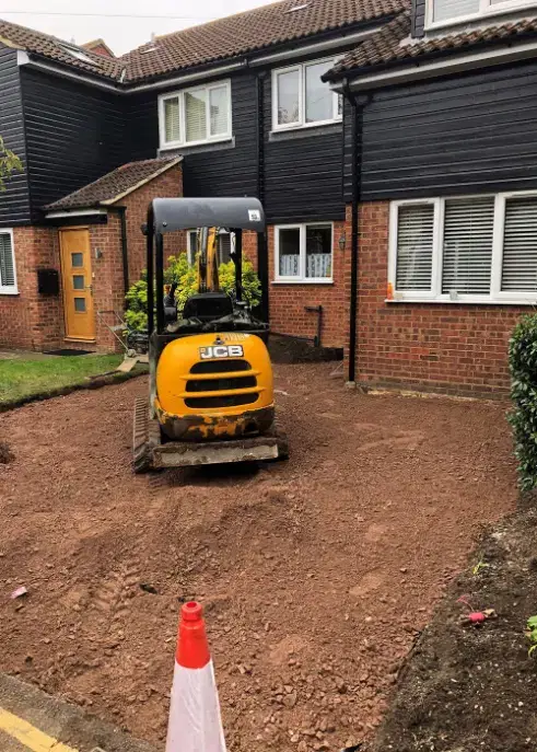 Baldock-Driveway-during_web Yellow JCB digger on a freshly dug driveway in front of a British semi-detached house with black cladding and brick walls.